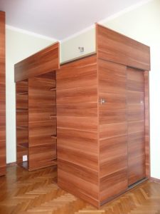Łóżko na wymiar umiejscowione na szafie z drzwiami suwanymi oraz otwartymi regałami na książki